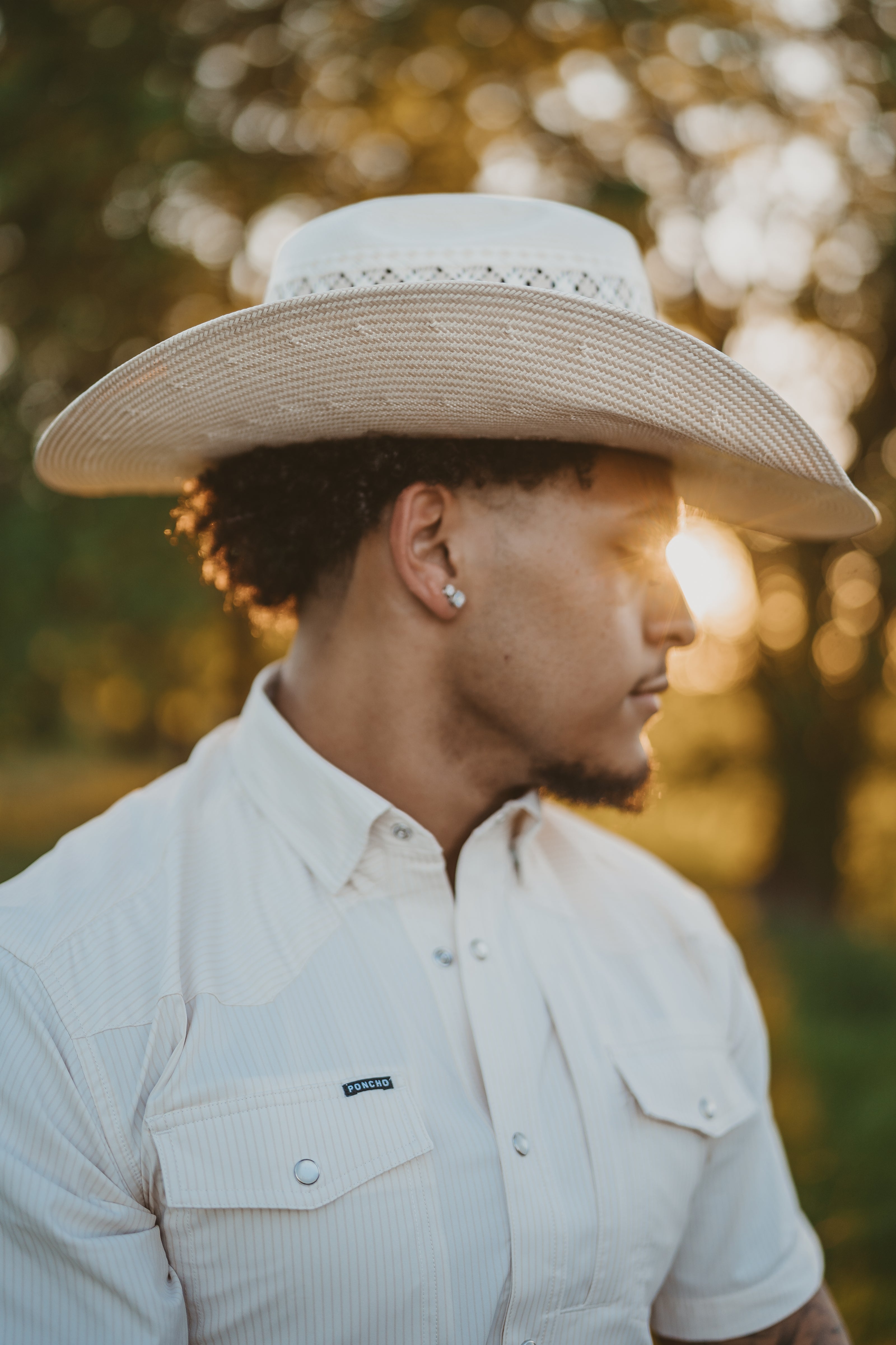 Man wearing a wide-brimmed hat and light-colored shirt outdoors with a blurred background