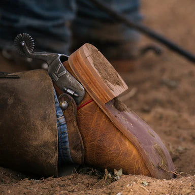 Brown leather boot with wooden spurs on a dirt ground