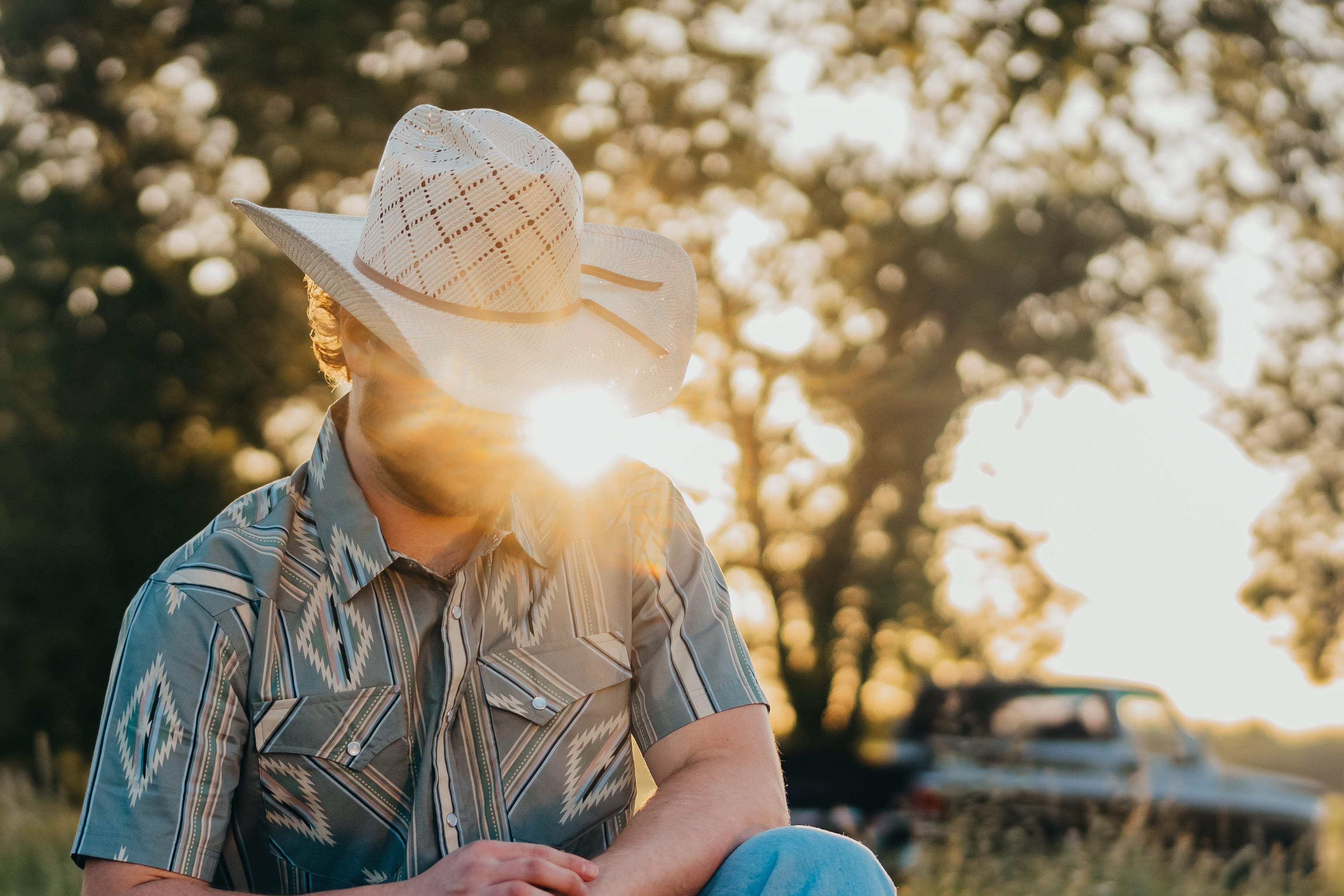 Person in cowboy hat sitting on rocks in a natural setting with sunset.