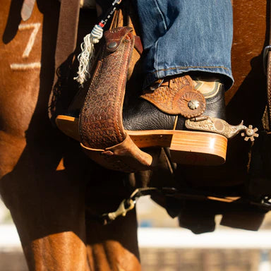 Close-up of a person wearing cowboy boots with a detailed brown boot strap and decorative buckle.