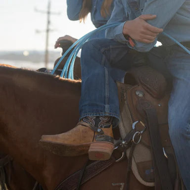 Person riding a horse wearing cowboy boots and a denim jacket.