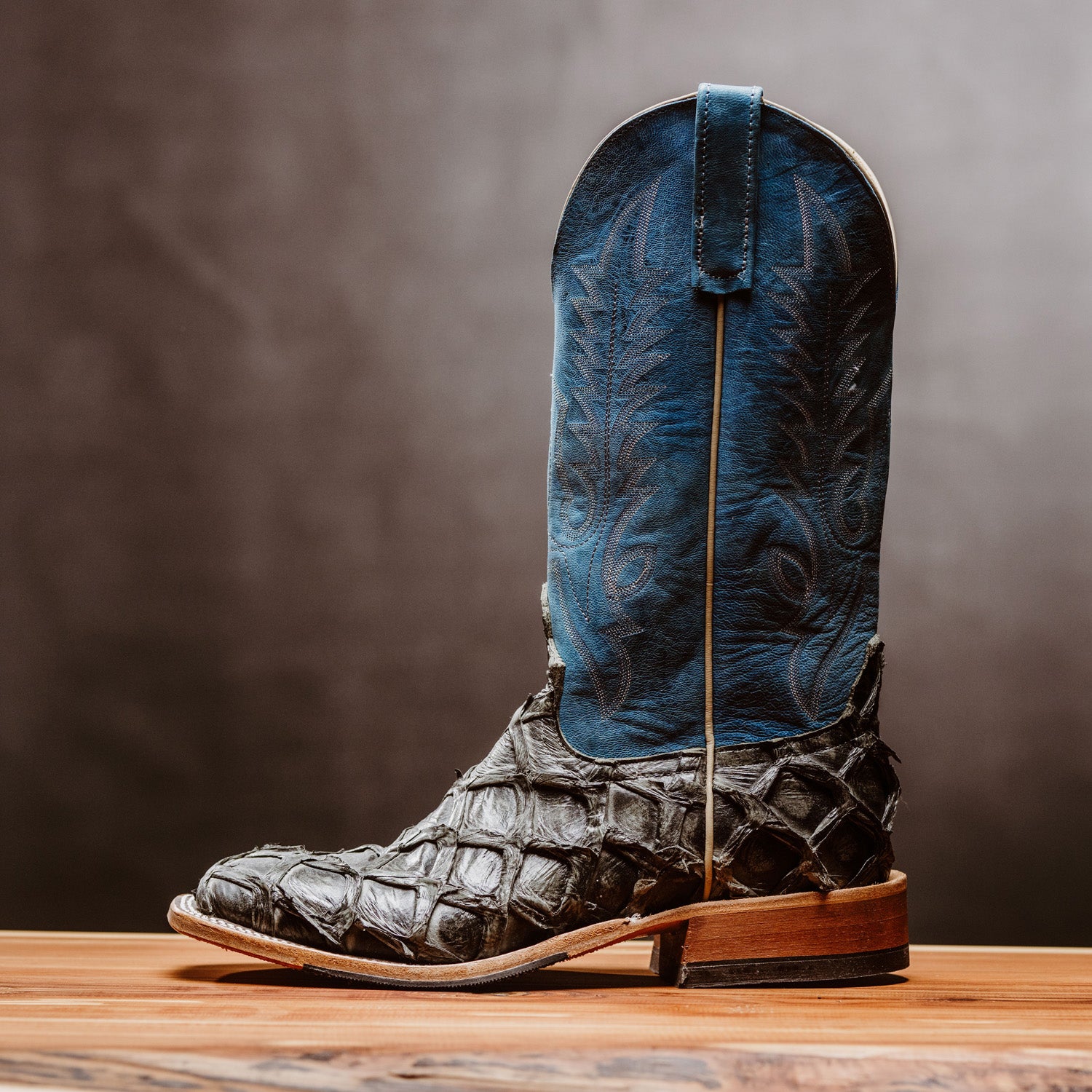 Blue and brown cowboy boot on a wooden surface with a dark background