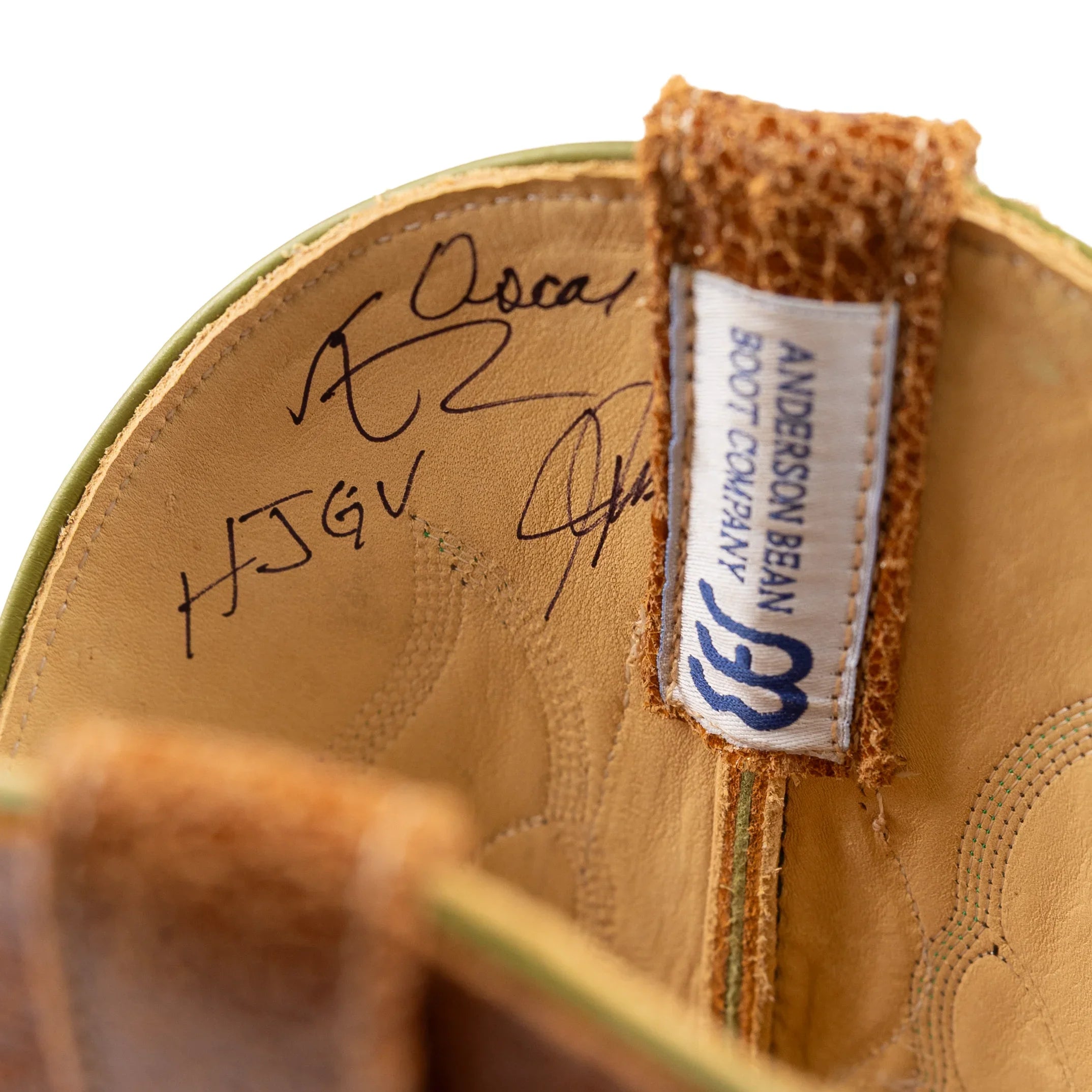 Close-up of a leather boot with a brand label and signature on a white background
