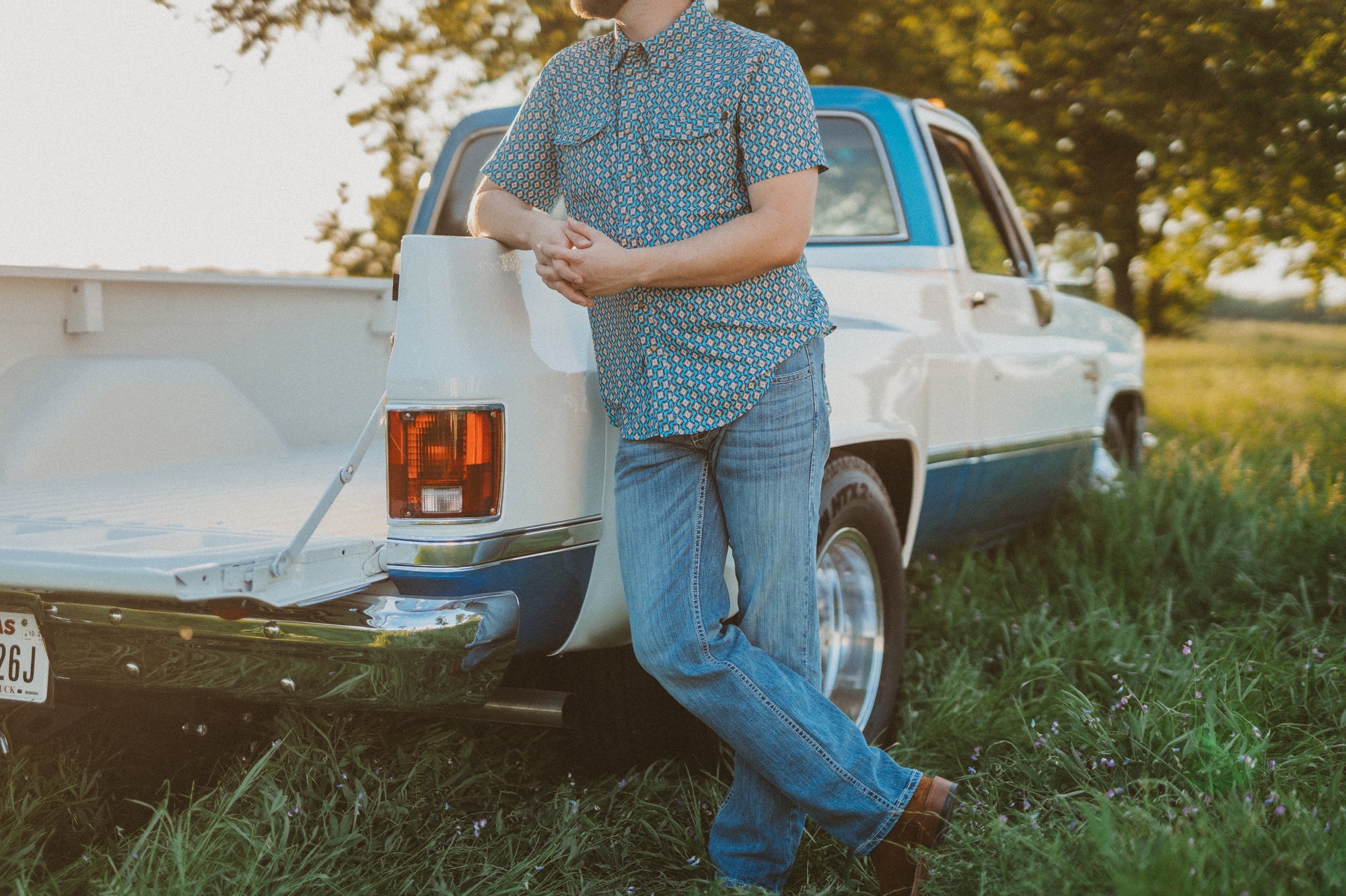 Person standing next to a vintage truck in a grassy field