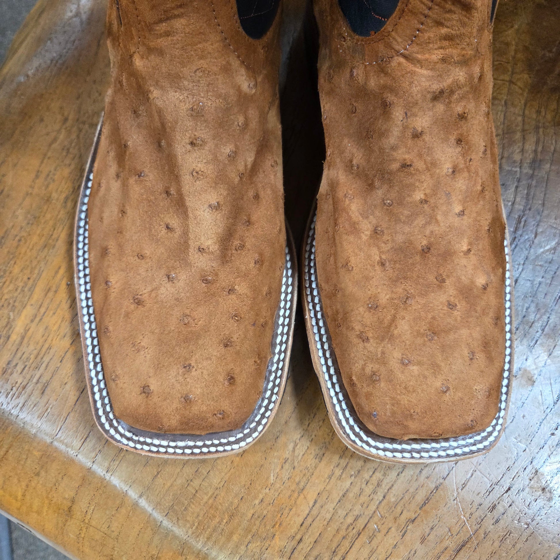 Pair of brown leather shoes with silver stitching on a wooden surface