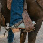 Close-up of a horse's leg with a brown leather girth and blue jeans.
