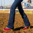 Person wearing blue jeans and red shoes standing on a dirt field with blurred background